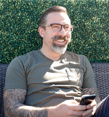 Man wearing Splinter Johnny Fly sunglasses with acetate front section and wooden arms, sitting outdoors smiling while holding a smartphone.